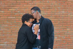 engaged-couple-holding-each-other-in-front-of-a-brick-wall-sharing-a-light-moment