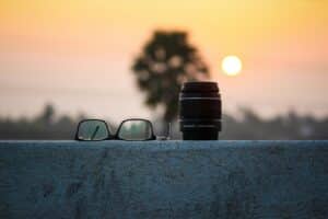 glasses and a camera lens on a concrete slab sunset in the background